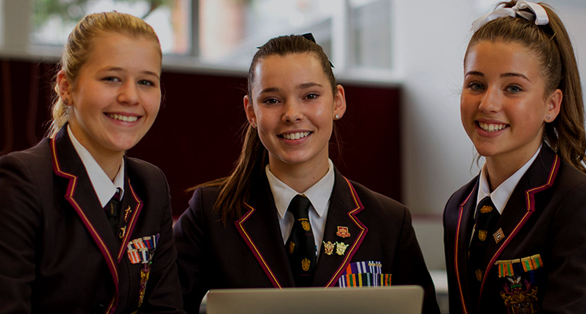 three haileybury students smiling at a laptop